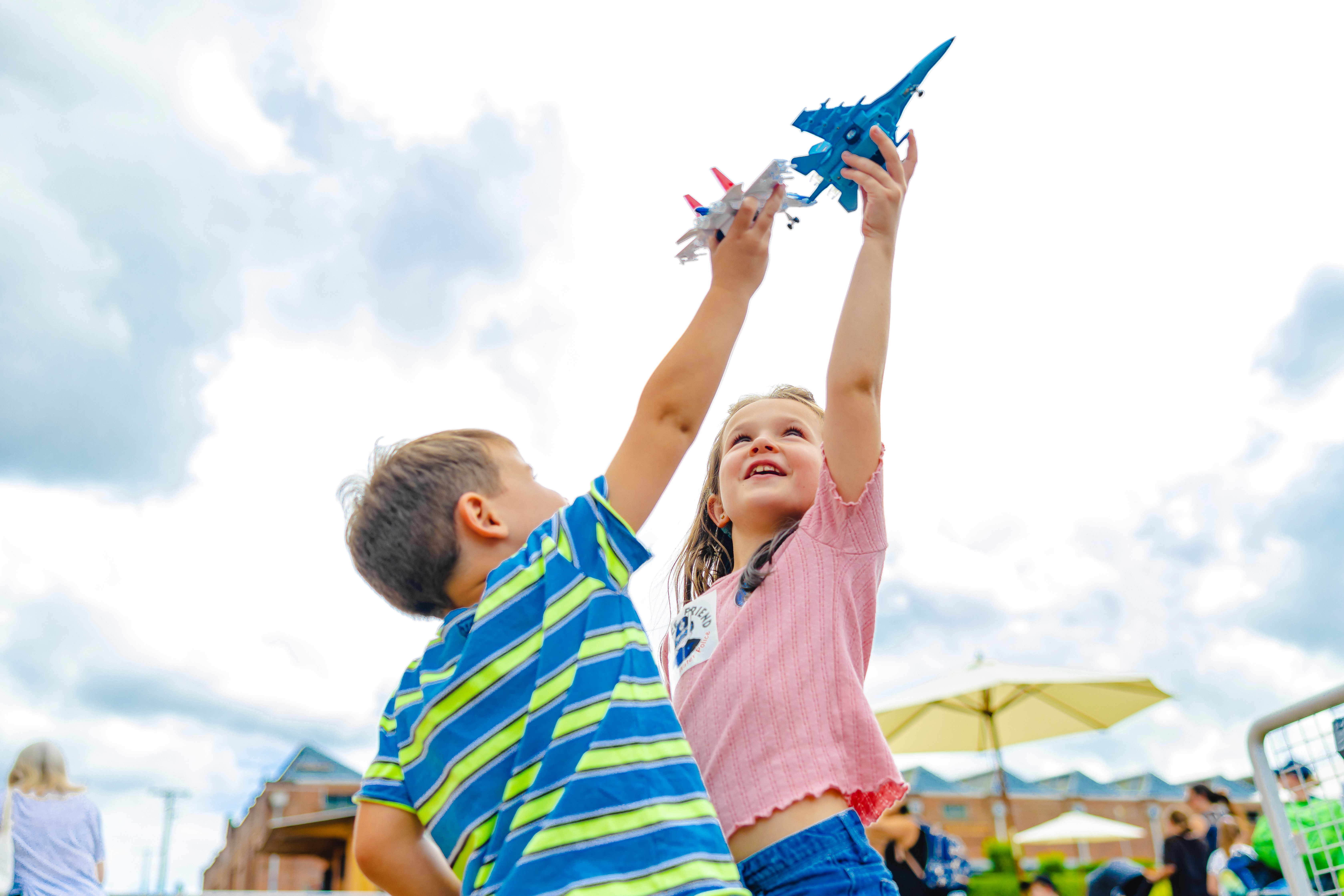 Two young pointing their toy planes to the sky